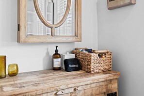 A wooden vanity with a mirror, a bottle of lotion, a black makeup bag, and a woven basket. - Belclare - Vineyard Estate (Northport)
