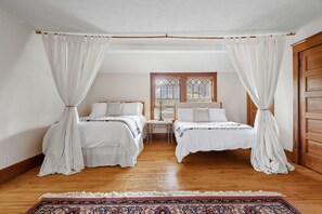 Ein Zimmer mit zwei Betten, Holzboden, einem Fenster mit Blick und einer Tür.