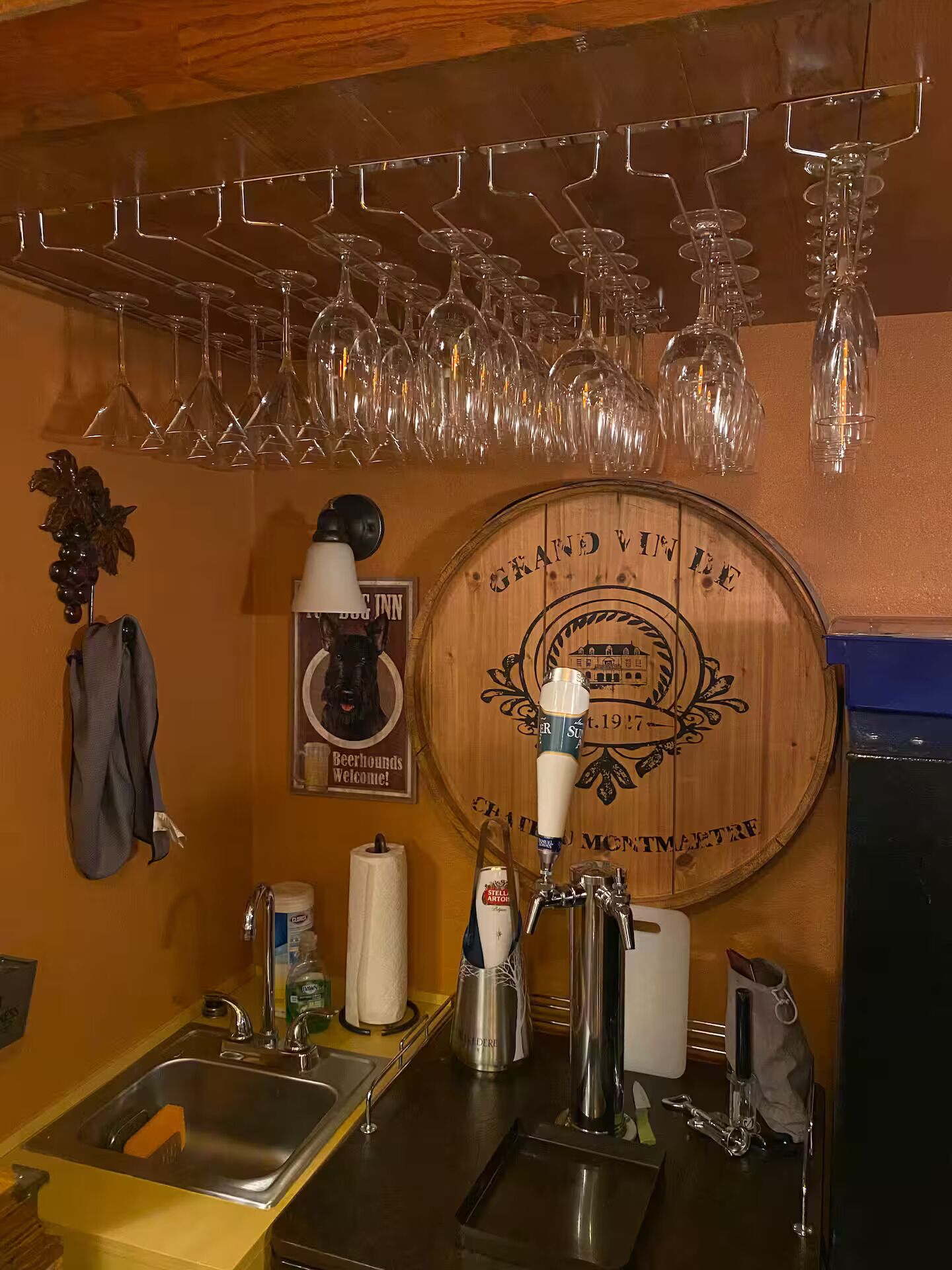A bar area with a wooden wall, a beer tap, and a wine glass rack.