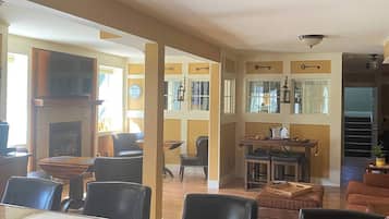 A dining area with a wooden table, chairs, and a fireplace. There are multiple windows and a ceiling fan.