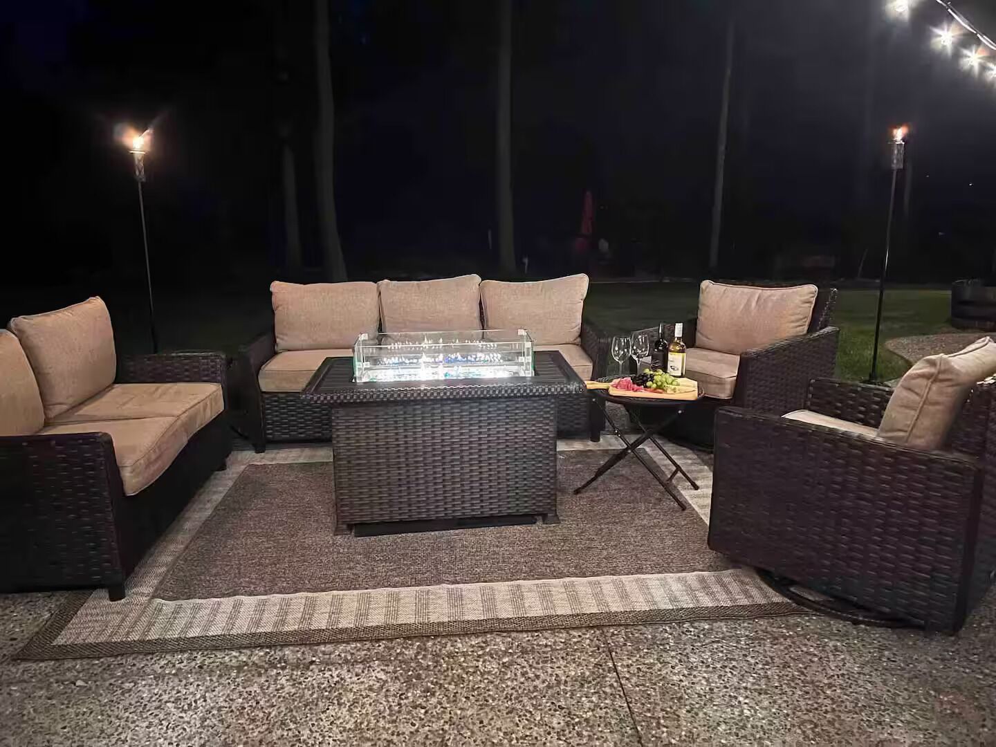 An outdoor seating area with a glass-top table, cushioned chairs, and a fire feature.