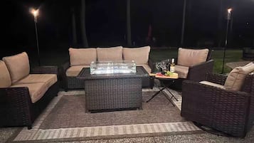 An outdoor seating area with a glass-top table, cushioned chairs, and a fire feature.