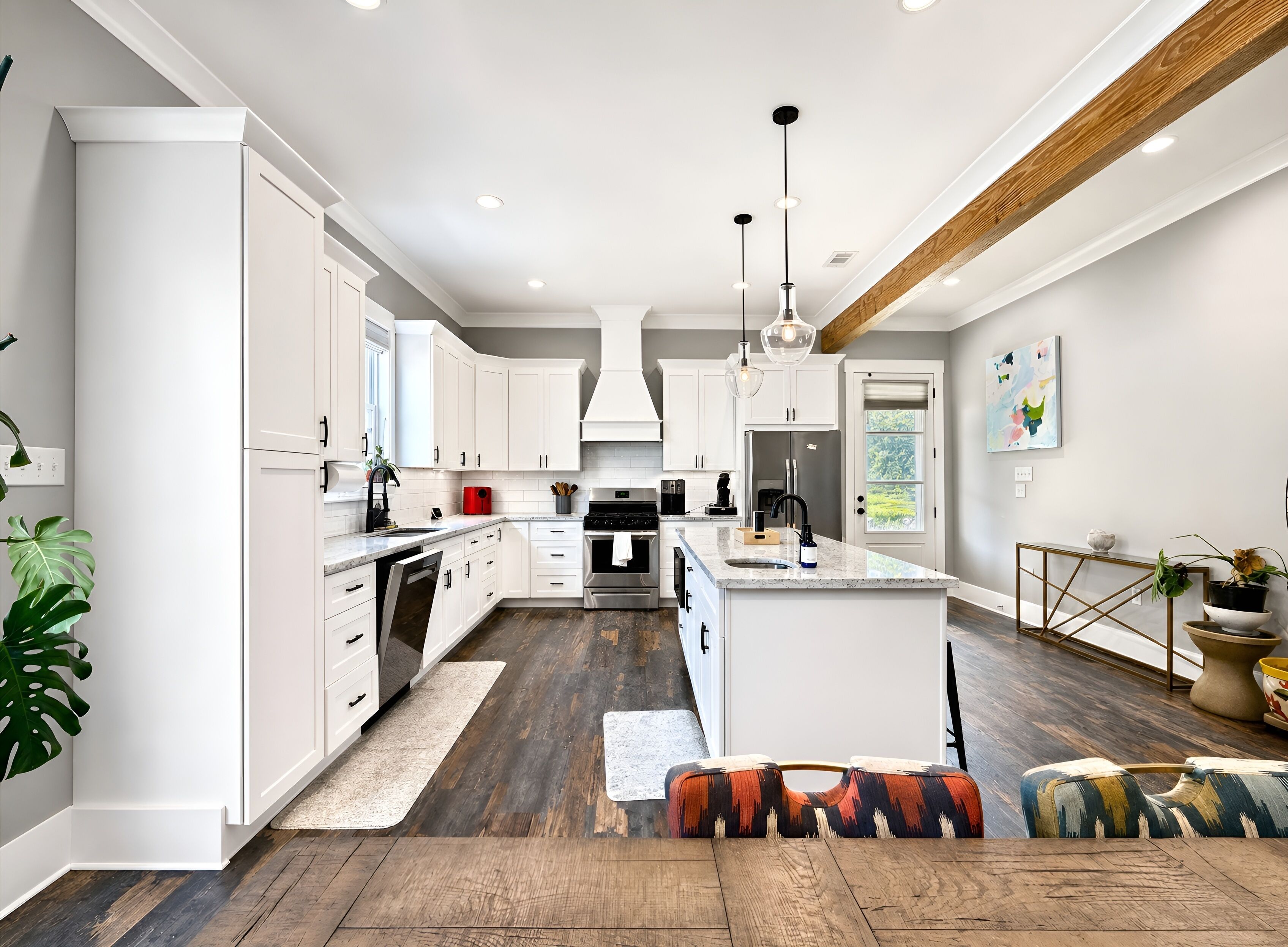 Une cuisine moderne avec des meubles blancs, un îlot central et une poutre en bois au plafond.