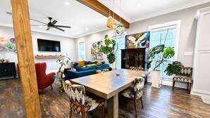 A modern living room with a wooden dining table, red armchair, blue sofa, and a ceiling fan. - The Seaglass Bungalow - Where Colorful Comfort Meets Gulf Coast Charm (Gulfport)