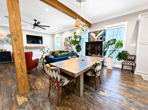 A modern living room with a wooden dining table, red armchair, blue sofa, and a ceiling fan. - The Seaglass Bungalow - Where Colorful Comfort Meets Gulf Coast Charm (Gulfport)