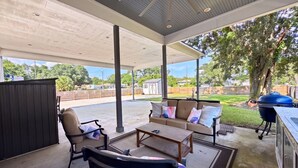 An outdoor patio with a covered seating area, a grill, and a view of the neighborhood. - The Seaglass Bungalow - Where Colorful Comfort Meets Gulf Coast Charm (Gulfport)