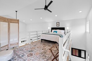 A bedroom with a bed, a ceiling fan, a patterned rug, and a white railing.