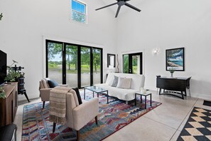 A spacious living room with a large window, a ceiling fan, a sofa, a coffee table, and a painting on the wall.