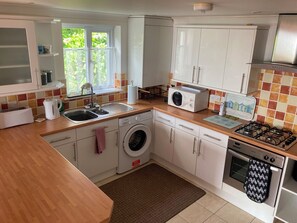 A modern kitchen with white cabinets, a washing machine, a stove, and a microwave. - Tide Watch (Penzance)