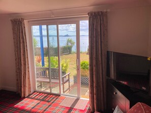 A room with a television, a sliding glass door to a balcony, and a plaid carpet. - Tide Watch (Penzance)