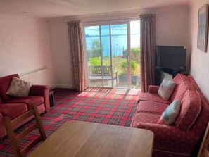 A living room with a red plaid carpet, two red sofas, a wooden coffee table, and a television on the wall. - Tide Watch (Penzance)