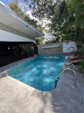 A swimming pool with a concrete deck, surrounded by a stone wall and greenery. - Hotel Wilson Anexo (Liberia)