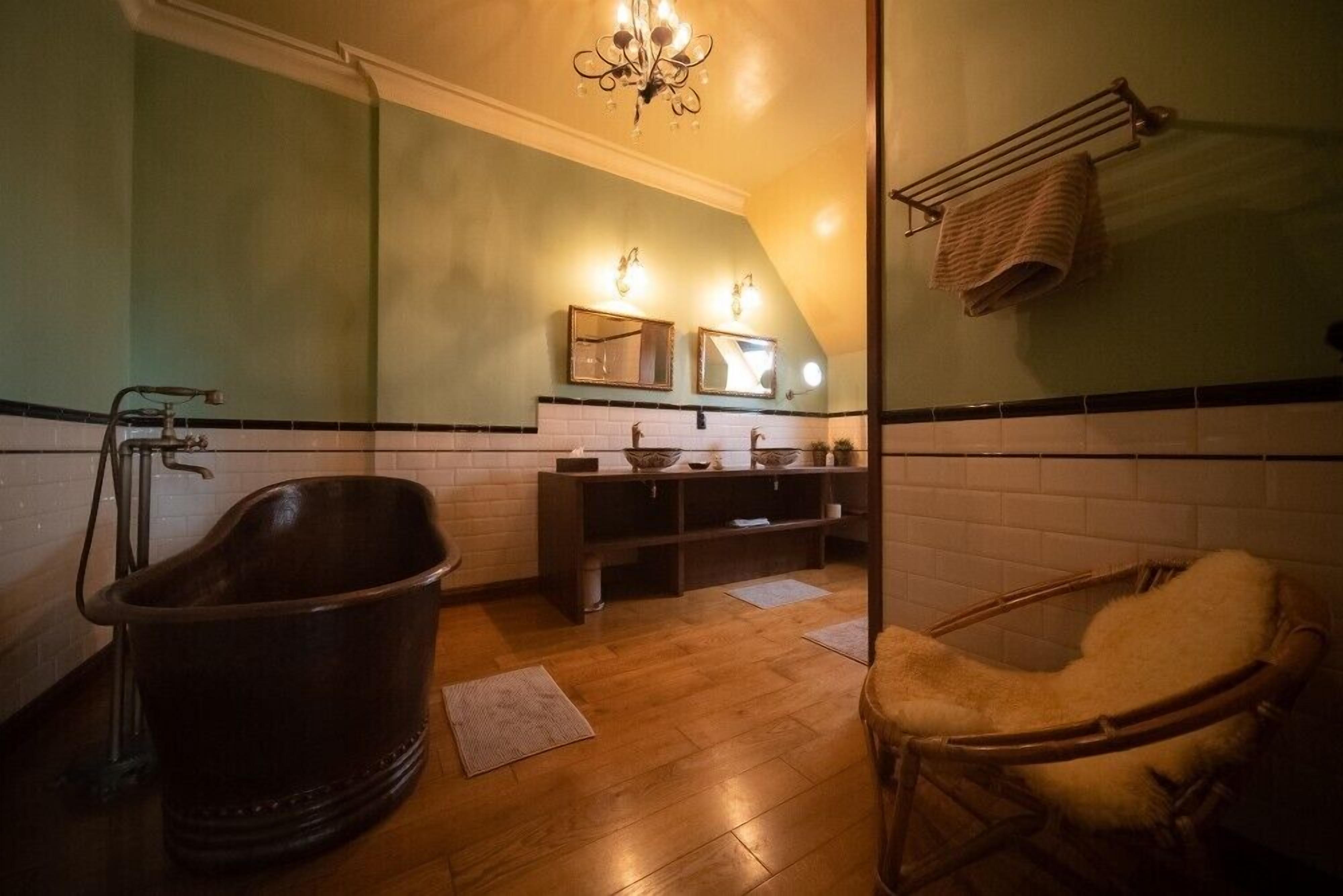 A bathroom with a bathtub, a wooden chair, a vanity with mirrors, and a towel rack.