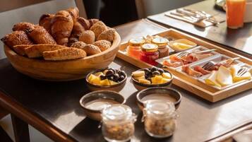 A breakfast buffet with pastries, fruits, cheeses, meats, and condiments.
