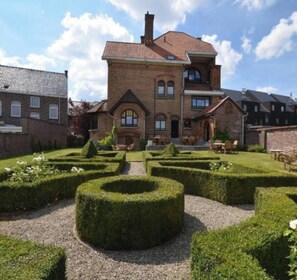 A large brick building with a symmetrical garden featuring circular hedges and a gravel path.