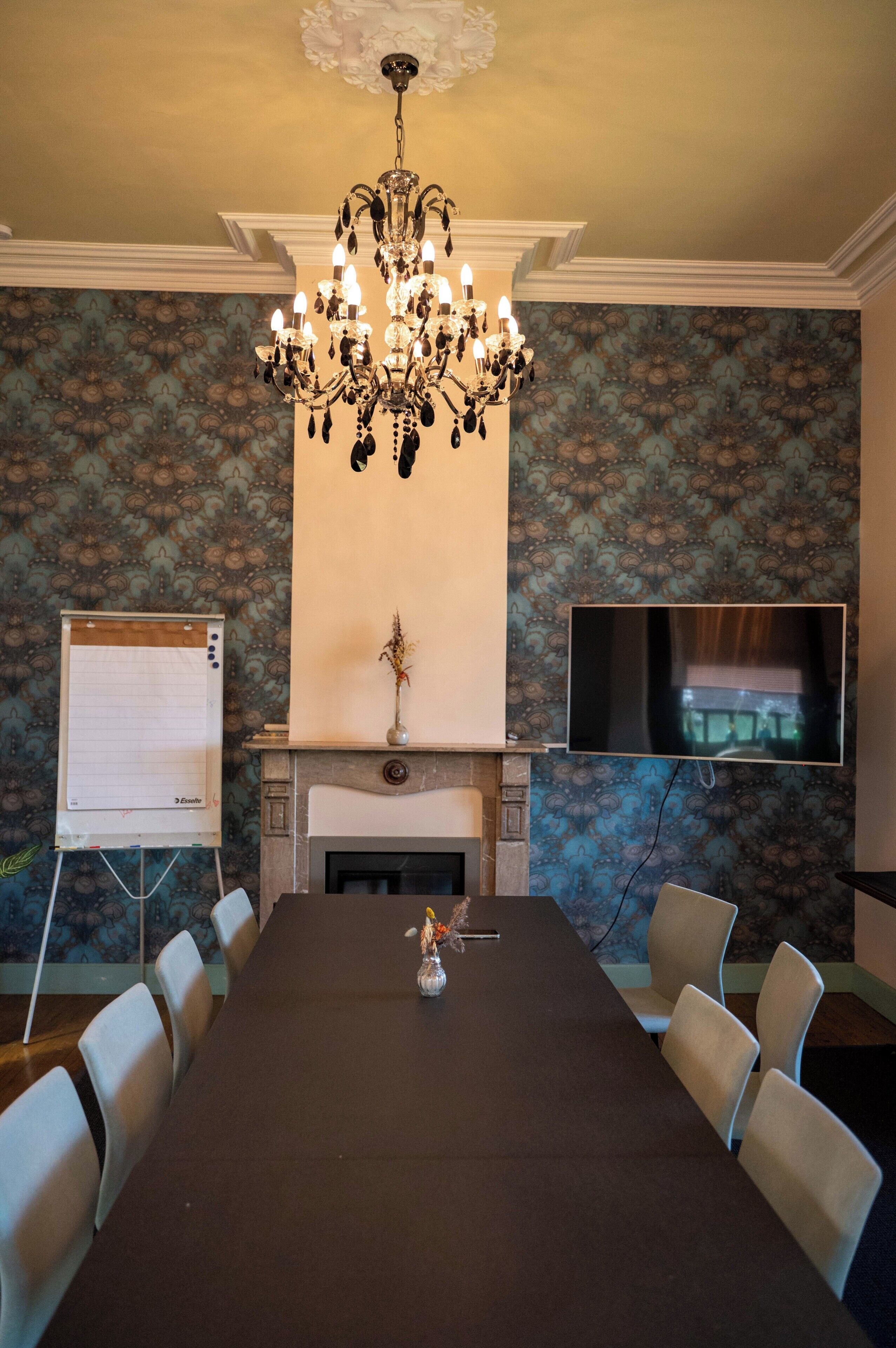 A conference room with a long table, chairs, a chandelier, a whiteboard, a fireplace, and a television.
