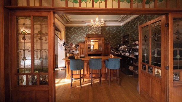 A wooden interior with a bar area, bar stools, and a chandelier. - Villa Clementine (Kruishoutem)