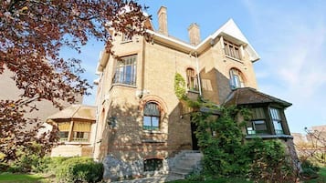 Une maison à deux étages avec une façade en pierre, un porche à l’avant et un petit jardin devant.