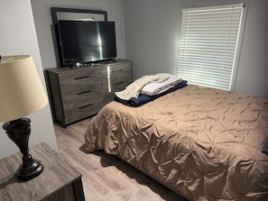 Un dormitorio con cama, cómoda, televisor y lámpara.