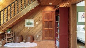 A wooden staircase leading to a loft bedroom with a sloped ceiling, a wooden door, a bookshelf, and a framed picture on the wall.