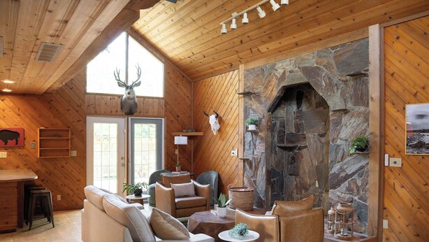 A cozy interior with a stone fireplace, wooden walls, and a seating area with leather sofas and chairs.