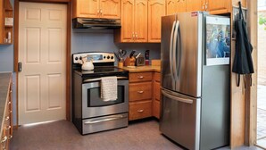 A compact kitchen with a stainless steel refrigerator, a built-in oven, wooden cabinets, and a small countertop.