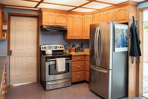 A compact kitchen with a stainless steel refrigerator, a built-in oven, wooden cabinets, and a small countertop.