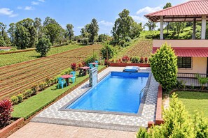 A swimming pool with a tiled deck, surrounded by a landscaped garden with a view of a vineyard. - Classic Jungle Eye (Mahabaleshwar)