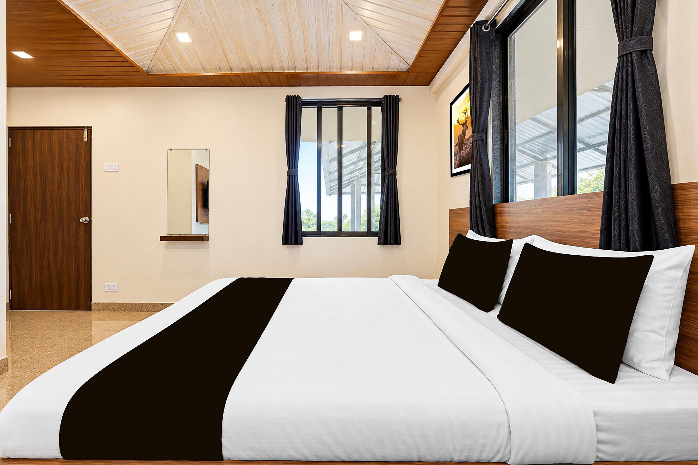 A modern hotel room with a large bed, a wooden ceiling, a window with curtains, and a painting on the wall.