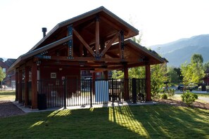 Un pavillon en bois, doté d’un toit incliné, entouré d’une clôture métallique, situé dans une zone herbeuse avec des montagnes en arrière-plan.