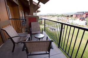 A balcony with two wicker chairs and a small table, overlooking a grassy area and buildings. - CW BLOCK Steamboat 2br (Steamboat Springs)