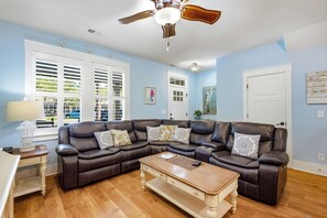 Ein Wohnzimmer mit einem braunen Ledersofa, einem Holztisch und einem Deckenventilator.