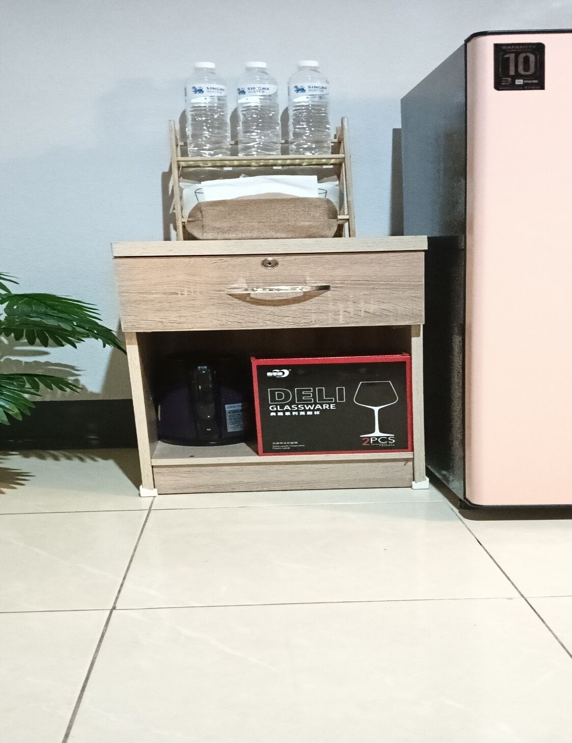 A wooden nightstand with a drawer, a glassware box, and a refrigerator.