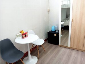 A small room with a white table, two chairs, a black cabinet with a kettle and water bottle, and a wooden door.