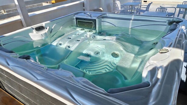 A hot tub with a clear interior, surrounded by a wooden deck and outdoor furniture. - A brand-new facility in the center of Pulsano (TA), opening in July 2026! (Pulsano)