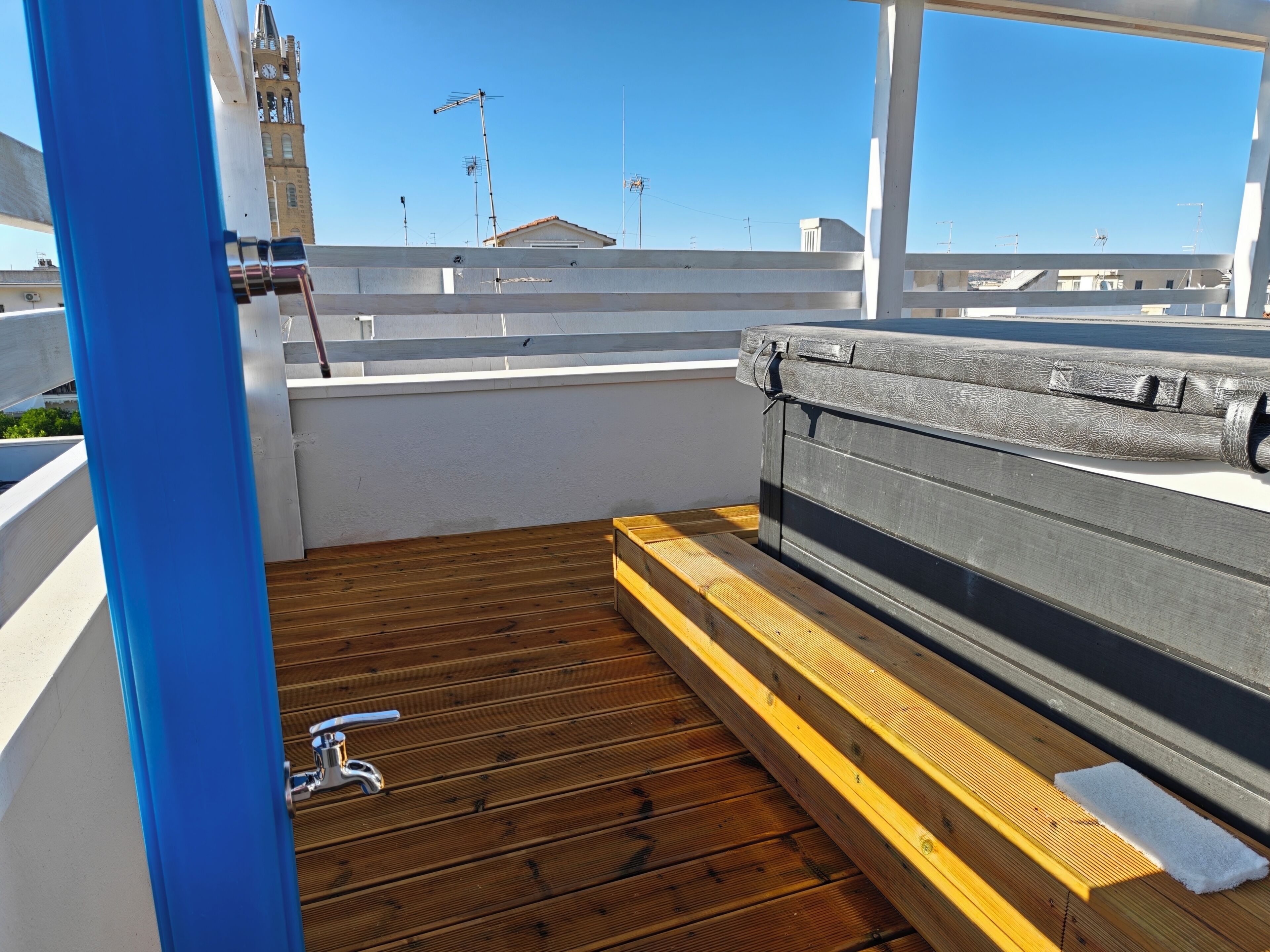 Une terrasse sur le toit avec une plateforme en bois, un jacuzzi et une vue sur les bâtiments en arrière-plan.