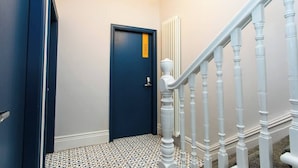 A hallway with a blue door, white railing, and patterned floor tiles.