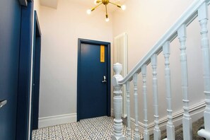 A hallway with a blue door, white railing, and patterned floor tiles.