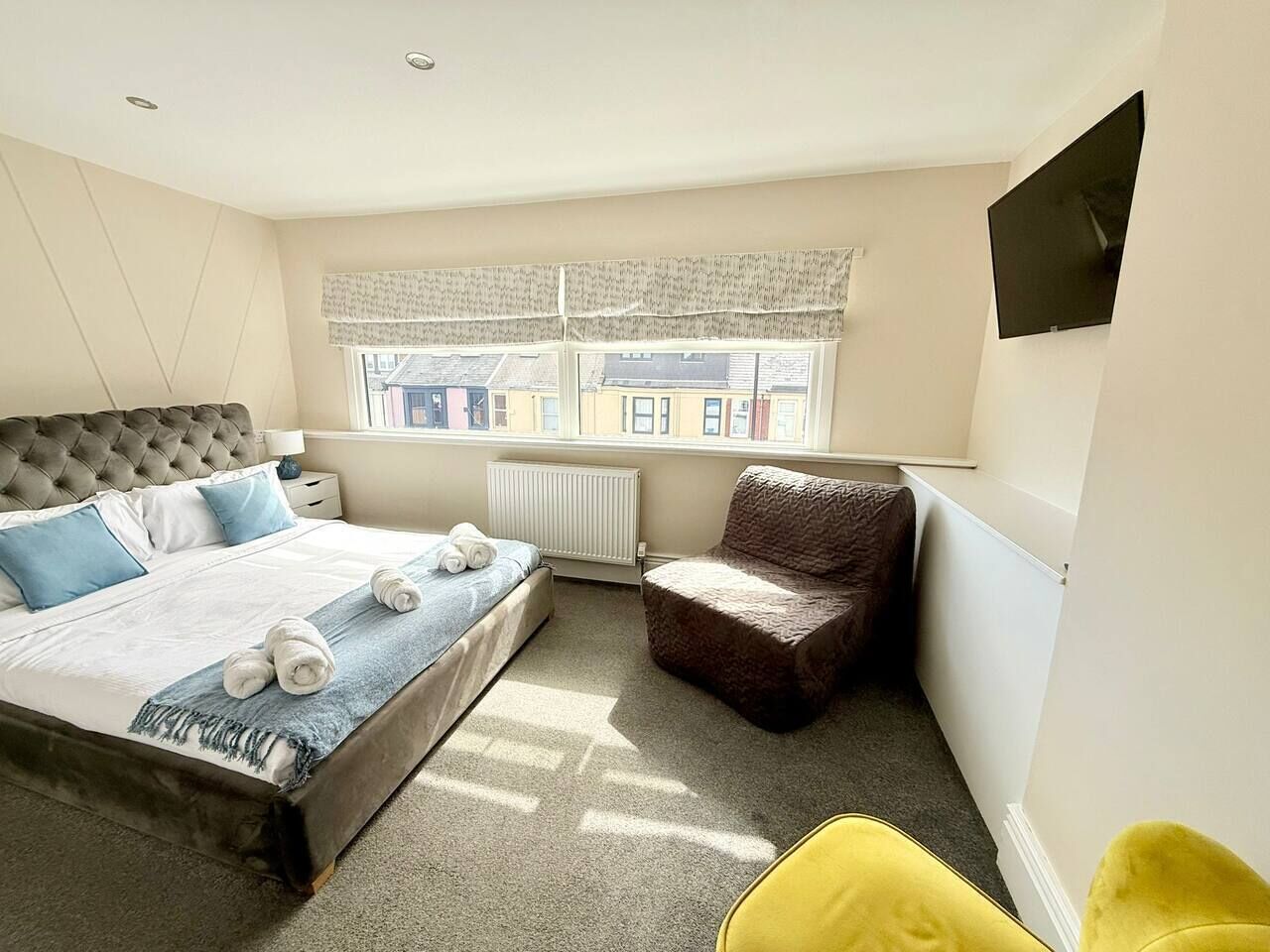A bedroom with a bed, a chair, a radiator, and a window with curtains.