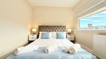 Une chambre d’hôtel avec un grand lit, deux tables de chevet avec des lampes, une fenêtre donnant sur un beau paysage et un radiateur.