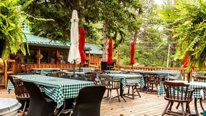 Een buiten-eetgedeelte met tafels, afgedekt met geruit tafelkleed, omringd door houten stoelen en rode parasols.