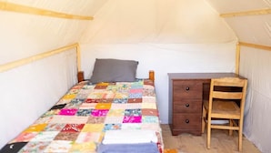 Een tent met een enkel bed, een houten bureau en een stoel.
