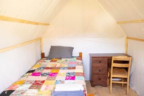 Ein Zelt mit einem Einzelbett, einem Holztisch und einem Stuhl.