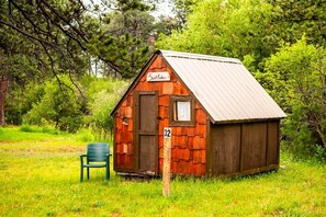 A small wooden cabin with a metal roof, a sign reading 'Sant Kater', and a number '32' on a post. - Saint Kateri Mini Cottage (Story)