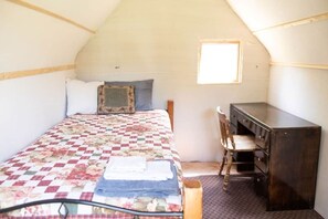 A small, cozy room with a bed, a desk, and a chair. - Saint Kateri Mini Cottage (Story)