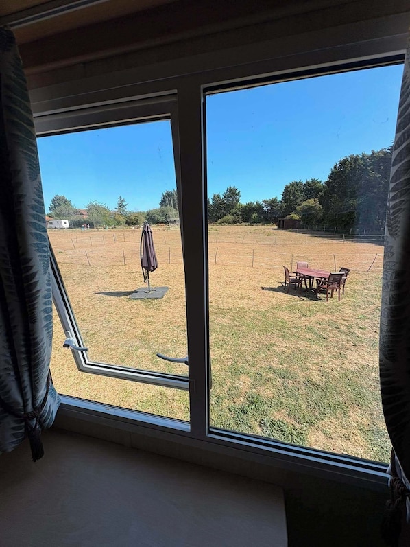 A room with a large window overlooking a grassy outdoor area with a picnic table and umbrella. - Luxury Caravan - Adults Only (Mablethorpe)