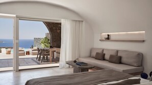 A modern bedroom with a sofa, a small table, and a view of the ocean. - Elyrion Suite, Divine Sea Views, Private Pool, Furnished Terrace, Sanrotini (Oia, Santorini)