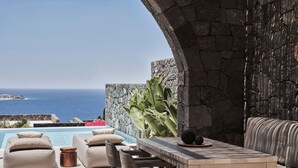 An outdoor seating area with a pool, stone wall, and a view of the sea. - Elyrion Suite, Divine Sea Views, Private Pool, Furnished Terrace, Sanrotini (Oia, Santorini)