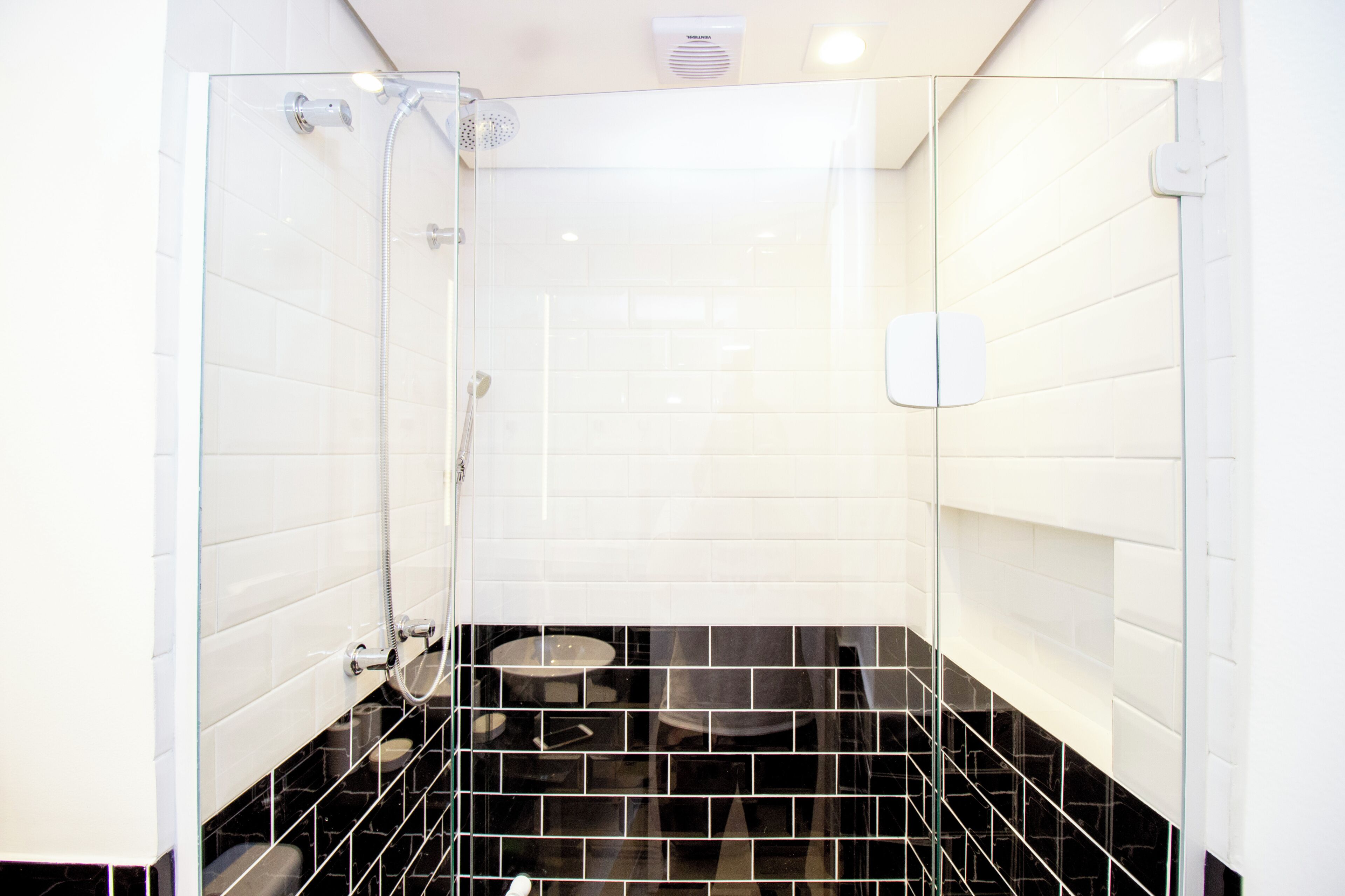 Un baño moderno con ducha envuelta en vidrio, paredes de azulejos blancos y suelo de baldosas negras.