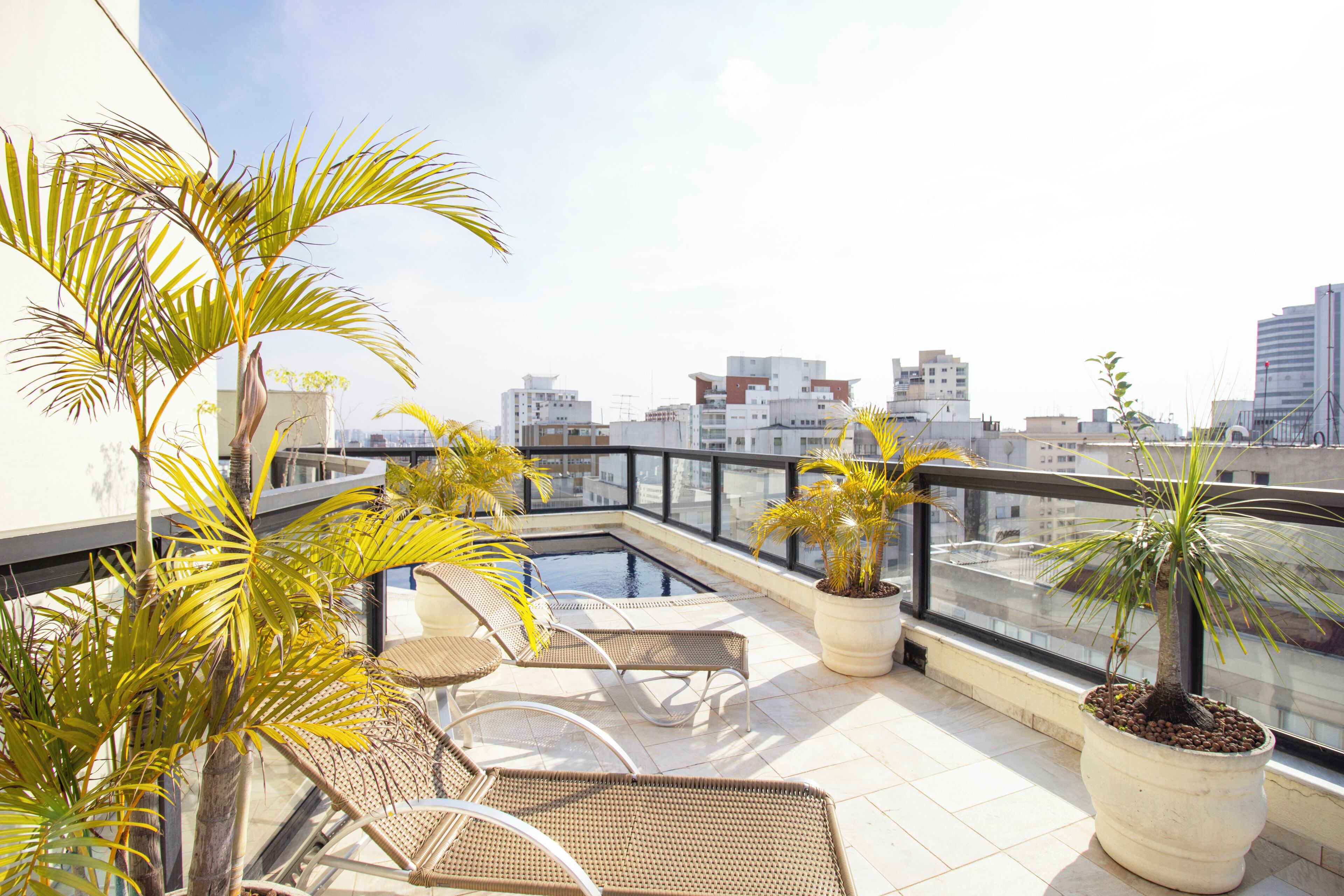 Terraço no telhado com piscina, espreguiçadeiras e plantas em vasos.